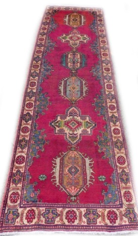 A Persian runner, with a design of medallions on a red ground, one wide border, 325cm x 98cm.