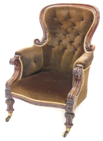 An early Victorian mahogany show frame armchair, with a button padded back and sides, scroll carved arms supports on turned and leaf carved legs with brass casters.