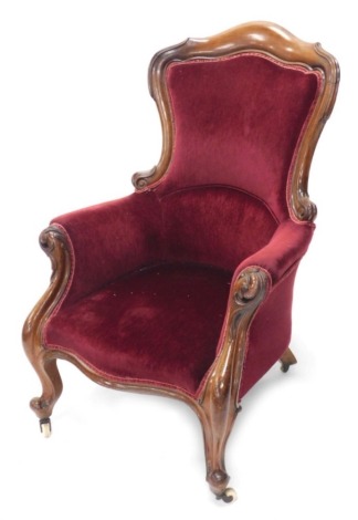 A Victorian mahogany show frame armchair with a padded back, arm rest and seat with scroll carved arm supports and legs and terminating with ceramic casters.