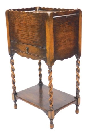 A 1920's oak work table, the raised top with double sliding compartments enclosing a recess, above a frieze drawer on spiral turned supports with under tier, 77cm high, 43cm wide.