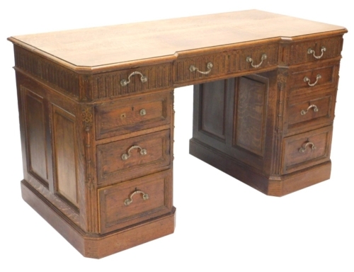 An early 20thC oak desk, the top with a moulded edge above an arrangement of three frieze drawers, each carved with flutes, above three further panelled doors, each pedestal flanked by split turned pilasters on a plinth, 141cm wide.