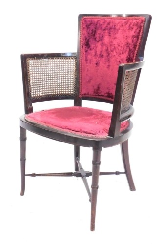 A mid 20thC mahogany framed bergere armchair, with over stuffed back and seat in crimson material on turned legs joined by an X stretcher, 89cm high.