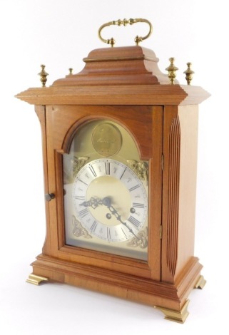 A mahogany cased mantel clock, with arched brass dial, silvered chapter ring with Roman numerals and brass spandrels formed as Amorini, the circular maker's plaque marked D J Hallwood Ely, with a caddy top and brass four point finials, on brass ogee brack