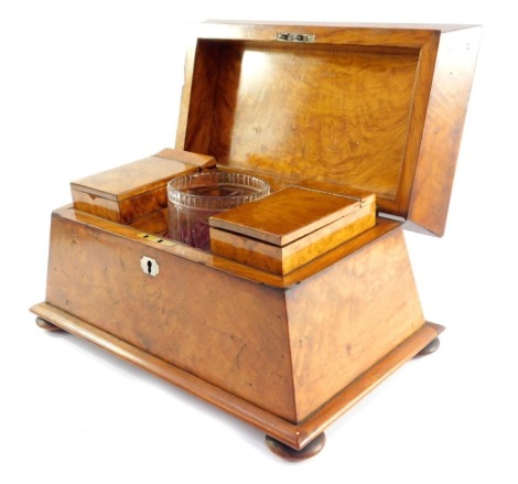 A Regency satinwood sarcophagus tea caddy, the hinged lid opening to reveal a pair of tea boxes, flanking a mixing bowl recess, with a cut glass mixing bowl, the box with mother of pearl key escutcheon, raised on bun feet, 23cm high, 39cm wide, 24cm deep.