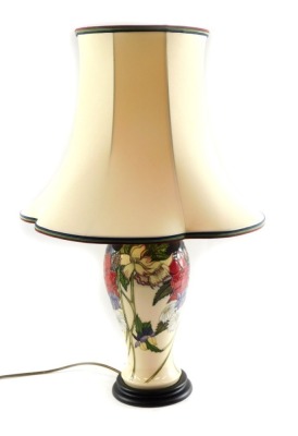 A Moorcroft pottery table lamp, of baluster form, decorated with mixed flowers against a cream ground, with shade, 67cm high.