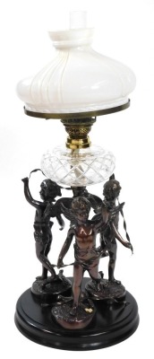 An early 20thC spelter oil lamp, cast as three standing cherubs with ribbons around a central spiral fluted column, raised on a circular ebonised base, with a cut glass reservoir, glass chimney and fluted milk glass shade, 81cm high.