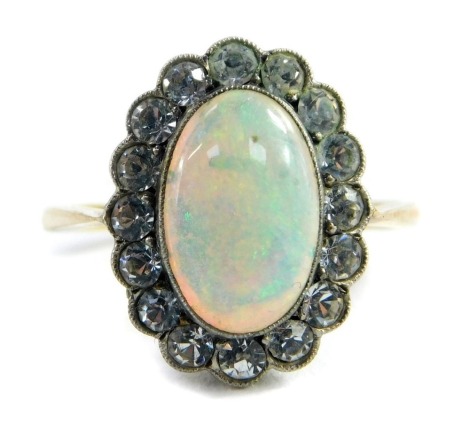A 9ct gold opal dress ring, the central oval opal in platinum rub over setting, surrounded by tiny white stones, on a raised basket setting, on yellow gold band marked 9ct and sil, size M, 2.5g all in, boxed. Auctioneer announce - description amended no