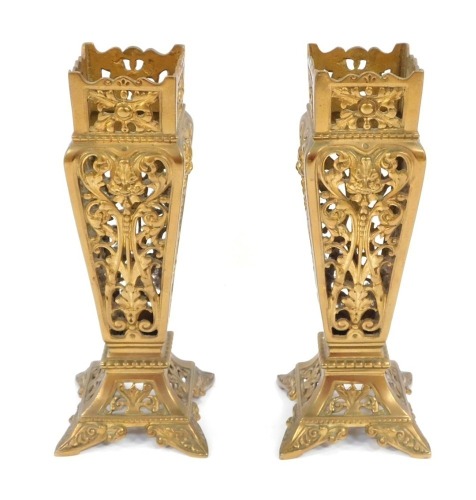 A pair of Victorian brass vase holders, each cast and pierced with scrolls and masks, of square section on flared bases, 21cm high.