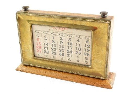 An early 20thC perpetual desk calendar, the rectangular top with paper inset, month dials and brass outer casing with turn dials stamped Manco Electroplate, on a wooden base, 13cm high, 21cm wide, 4cm deep.