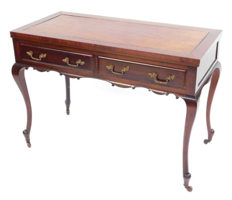 A Victorian mahogany writing table, the brown leather inset top, above two drawers with rococo style brass handles and carved apron, Raised on slender cabriole legs, on castors, 75cm high, 107cm wide, 50cm deep.