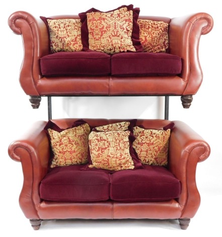 A pair of red leather two seater sofas, each with scroll arm supports and shaped sides, with two seat cushions and scatter cushion backs, on mahogany carved block feet, 73cm high, 165cm wide, 100cm deep.