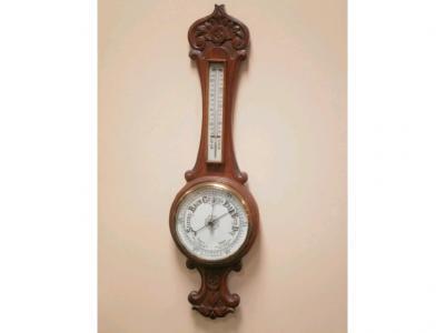 A late Victorian carved oak aneroid barometer with a thermometer over monochrome dial