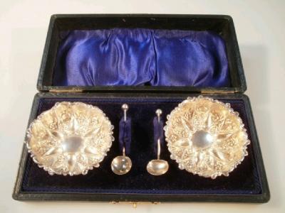 A pair of silver salts with spoons of circular design with three ball feet