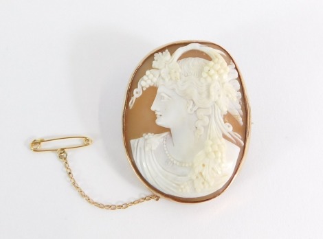A 19thC shell cameo brooch, with maiden in raised relief, with vines and grapes, in a rose gold border, marked 9ct, with single pin back and later safety chain, 4.5cm x 4cm, 17.6g all in.