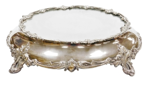 A Victorian silver plated wedding cake stand, with a mirrored top, the base decorated with vacant cartouches and scrolls, raised on four foliate scroll feet, 49cm diameter.