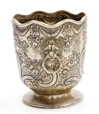 A Victorian silver bottle holder of Monteith form, with a waved rim, the body embossed with bows, swags, fruit, flowers and scrolls, with twin lion's head and ring handles, on a footed base, Daniel and John Welby, London 1898, 5½oz, 11cm high. - 2