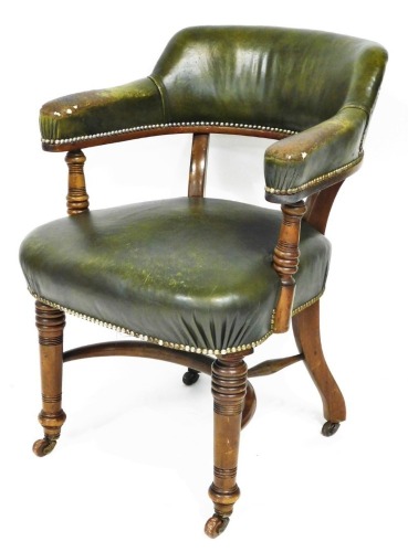 A late Victorian walnut library chair, upholstered in green leather with brass studded borders, on turned tapering legs with crinoline stretcher and ceramic castors.