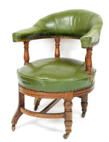 A 19thC oak revolving library chair, upholstered in green leather on turned supports on castors, 70cm diameter.