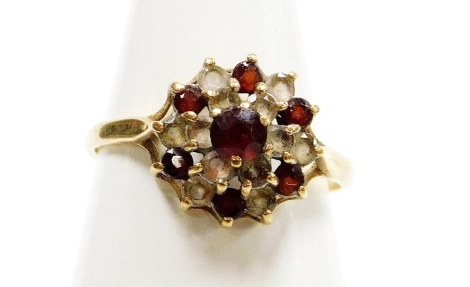 A 9ct gold dress ring, formed as a cluster set with layers of garnets and czs, on a raised basket, ring size O, 2.2g all in.