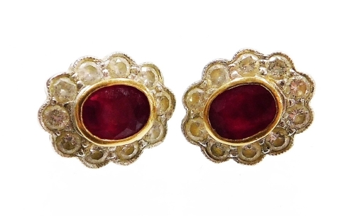 Withdrawn presale by vendor- A pair of ruby and diamond cluster stud earrings, the rubies in a rub over 18ct gold setting, surrounded by arrangement of twelve round brilliant cut diamonds, the studs 8mm wide, on yellow metal pin backs, 3.1g all in.