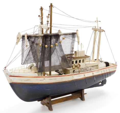 A carved wooden model of a fishing boat, fully rigged with nets, on a wooden stand, 45cm wide.