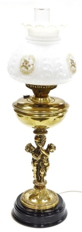 A brass oil lamp type electric table lamp, cast with a figural support, with clear glass chimney and moulded white glass shade, with reserves printed with flowers, 72cm high.