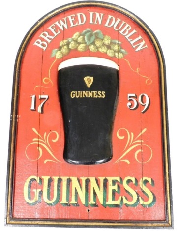 A wooden Guinness advertising sign, of arched form, Brewed In Dublin 1759, depicting a raised Guinness pint glass on a red ground, 92cm x 63cm.