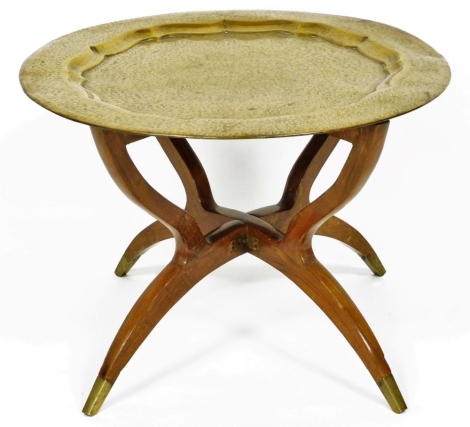 An Indian brass engraved tray, with raised border, on a folding hardwood stand with brass feet, 59cm diameter.