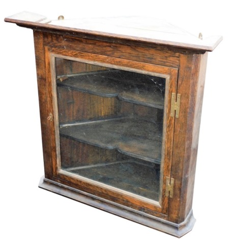 A George III style oak hanging corner cupboard, of small proportion, the carved top raised above a glazed door, on plain moulded base, probably early 20thC, 80cm high, 81cm wide, 45cm deep.