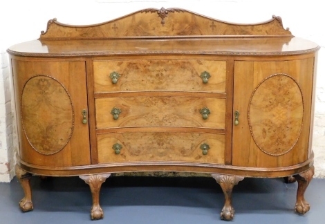 An early 20thC walnut kidney shaped sideboard, with a raised back, above a carved frieze with three drawers flanked by a pair of shaped doors each with oval panels on short cabriole legs headed by fans, with ball and claw feet, 112cm high, 180cm wide, 65c