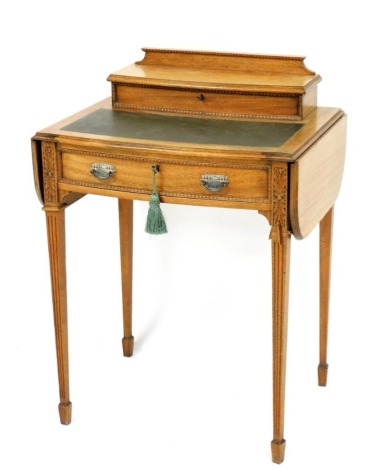 An Edwardian mahogany writing table, the bow fronted top with a hinged raised back enclosing a recess for letters, ink, etc., flanked by two drop leaves above a frieze drawer with beaded border, on square tapering reeded legs headed by floral patera, 187c