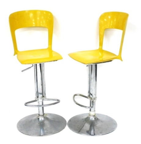 A pair of yellow moulded plastic and chrome plated bar stools, with a foot rest, on a domed base.