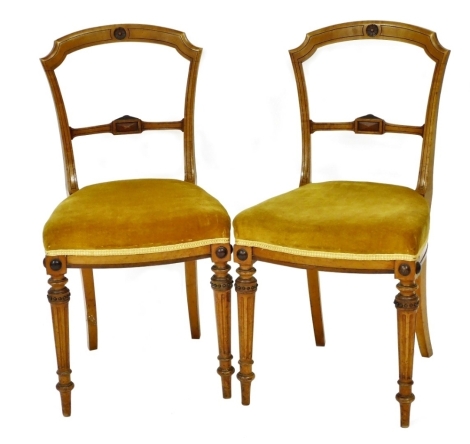 A pair of Victorian satin walnut side chairs, each with a shaped back and a padded seat upholstered in yellow fabric on turned and fluted legs.