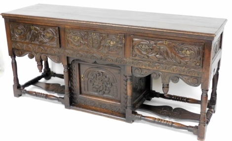 A late 19th/early 20thC oak dresser, the rectangular top with a moulded edge above three frieze drawers, profusely carved with flowers, leaves, etc., above a similarly carved apron with drop turned drop finials, above a panelled door, on turned supports a