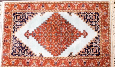 An Oriental rug, with a central lozenge shaped medallion in deep orange, on a turquoise ground with navy spandrels, one wide and two narrow borders, 155cm x 92cm.