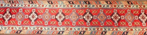 A Turkish runner, with a design of eleven alternating medallions, in blue on a red ground with two wide borders, 504cm x 90cm.