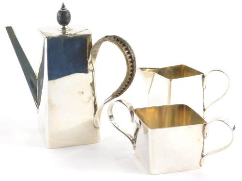 A Victorian silver three piece coffee service, by Hukin and Heath, possibly from a design by Dr Christopher Dresser, comprising coffeepot, milk jug and two handled sugar bowl, each of square form, the teapot with wicker handle, 13cm high, London 1896, 10o