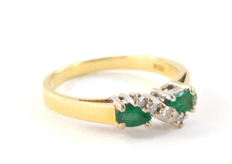 An 18ct gold emerald and diamond dress ring, set with two pear cut emeralds, each stone approximately 0.20cts, in a white four claw setting, with cross over central band set with three tiny diamonds, totalling approximately 0.05cts, on a yellow metal band