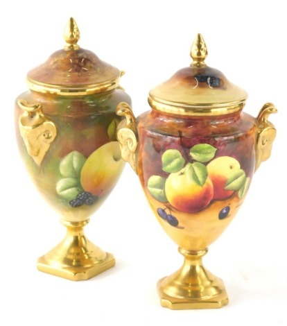 A pair of Coalport vases, by Higham and Goodwin, hand painted with fruit and gilt highlights, compressed lids, acorn finials, and gilt shaped feet, printed marks beneath, 20cm high. (2)