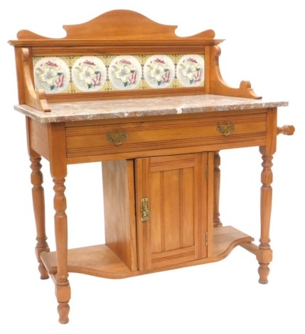 A Victorian walnut washstand, the raised back inset with floral printed tiles with a variegated marble top, the base with a frieze drawer above a panelled door, flanked by recesses on turned legs, 99cm wide.