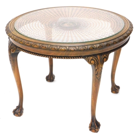 An early 20thC beech coffee table, with a circular cane and glass top and a leaf curled moulded edge above a gadrooned frieze on leaf and scroll cabriole legs and ball and claw feet, 80cm diameter.