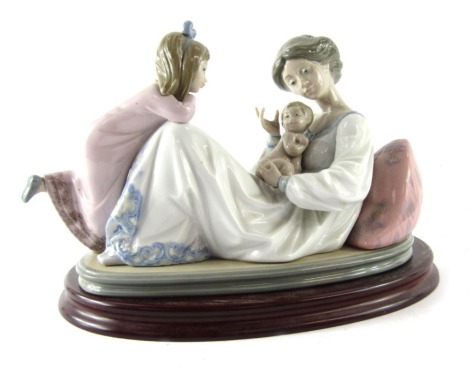 A Lladro porcelain figure group depicting mother and baby with child, no 1606, printed and impressed marks, on an oval wooden base, 20cm high, 23cm wide.