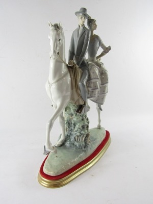 A Lladro porcelain figure group of a lady and gentleman riding on horseback, the gentleman in riding suit, with lady in a polka dot dress, mounted on a white horse, printed and impressed marks, on a gold and red plinth, 48cm high, 37cm wide. (AF) - 2