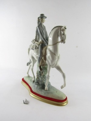 A Lladro porcelain figure group of a lady and gentleman riding on horseback, the gentleman in riding suit, with lady in a polka dot dress, mounted on a white horse, printed and impressed marks, on a gold and red plinth, 48cm high, 37cm wide. (AF) - 3