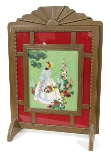 An Art Deco design fire screen, the embroidered centre depicting a crinoline lady carrying a basket of flowers, in a red outer border, with beaded detailing and sunburst design top, on fluted semi circular feet, 87cm high, 60cm wide, 26cm deep.