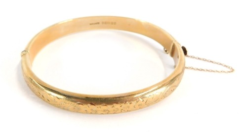 A 9ct gold hinged bangle, each size with engraved detailing and clip clasp, with 9ct gold safety chain, 12.7g all in, 7cm diameter.