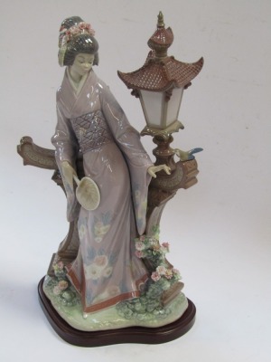 A Lladro porcelain figure of a Japanese geisha girl, modelled standing against a garden lantern, on a wooden base, 42cm high. - 2