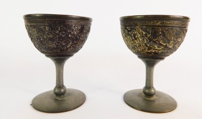 A pair of Chinese coconut beakers, each with pewter lined interior and stemmed foot, carved to the bowls with temples in a garden setting, two character mark, 10cm high.