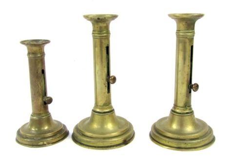 Three Victorian brass candle sticks, with lever candle adjustment, comprising a pair, 20cm high, and a single stick, 16cm high.