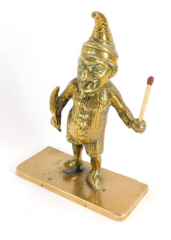 A Victorian Mr Punch novelty brass bar match striker, modelled in standing pose, holding a single match, raised on a rectangular base, 15cm high.